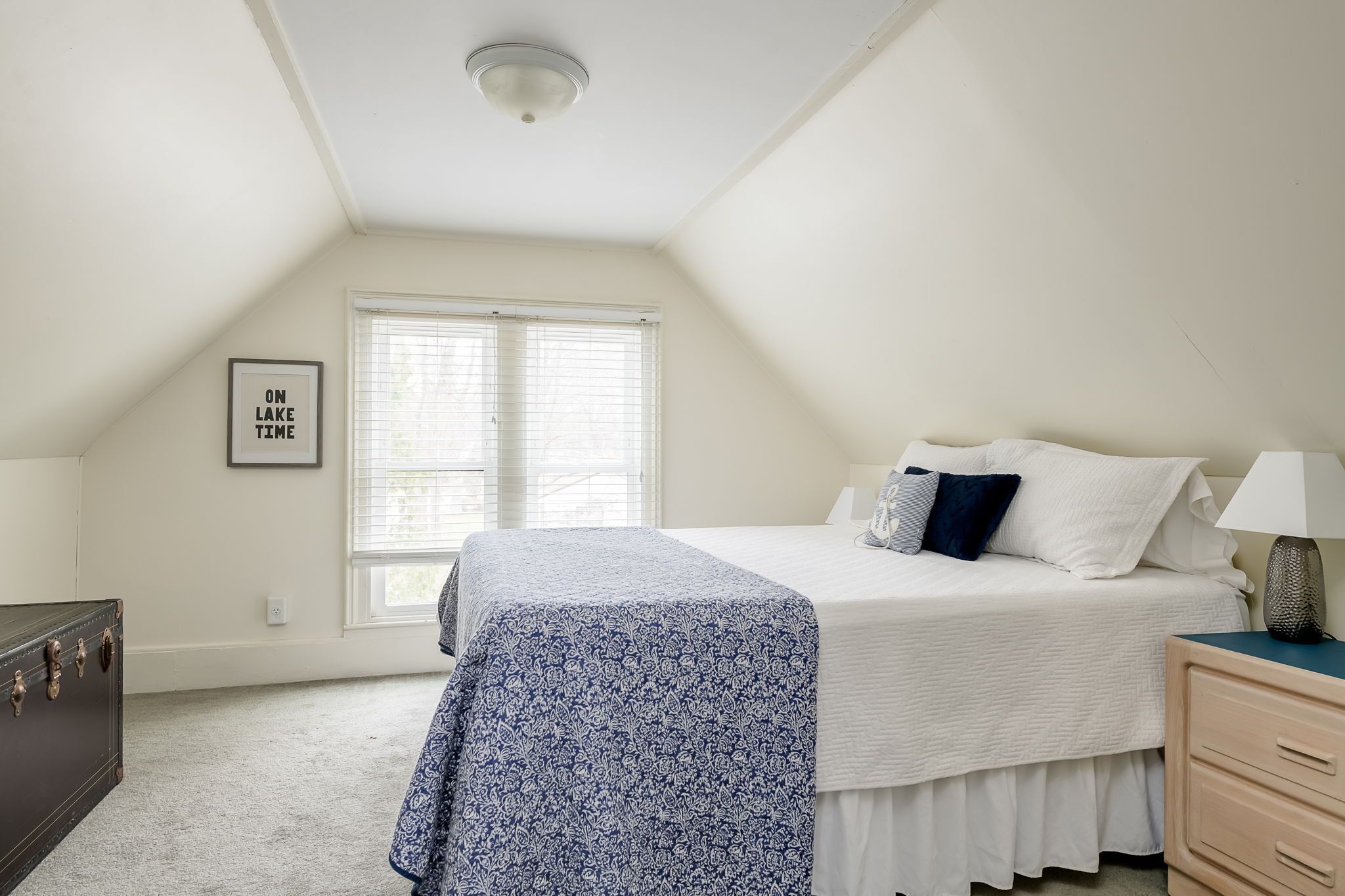 Un dormitorio con cama, cómoda, mesita de noche, lámpara y ventana con persianas.