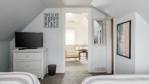 Un dormitorio con una televisión en una cómoda, una cama, una silla y un pasillo que conduce a otra habitación.