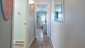 A hallway with a light blue wall, a wooden floor, and a door at the end. - Updated 1st floor, 1-bedroom, 2-Queen bed condo. Close to parks, beach, & boards (Ocean City)