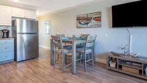 A kitchen with a stainless steel refrigerator, wooden dining table with chairs, and a flat-screen TV mounted on the wall. - Updated 1st floor, 1-bedroom, 2-Queen bed condo. Close to parks, beach, & boards (Ocean City)