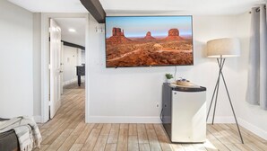 Una sala de estar moderna con un televisor de pantalla plana montado en la pared, una lámpara de pie y un mueble pequeño.