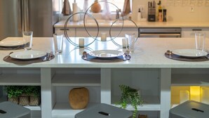 Una mesa de comedor dispuesta con platos, vasos y velas, con una cocina al fondo.