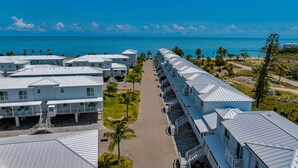 Una hilera de edificios de hotel blancos frente a la playa, con balcones, un cielo azul despejado y el océano al fondo.