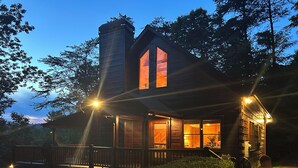 A wooden cabin with a large window, a chimney, and a porch with chairs.