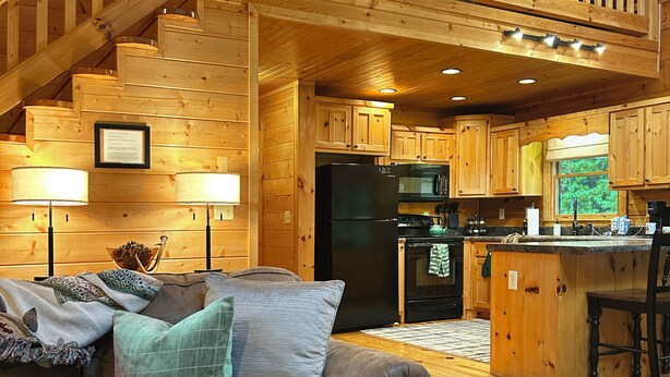 A cozy wooden cabin interior with a living room, kitchen, and staircase.