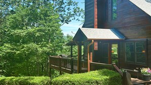 A wooden cabin with a covered porch, surrounded by lush greenery.