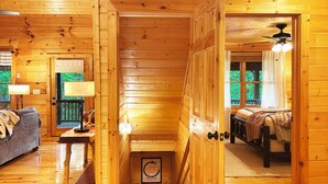 A wooden cabin interior with a sofa, a table, a bed, and a staircase.
