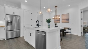 A modern kitchen with white cabinetry, stainless steel appliances, a central island with a sink, and pendant lighting. - Saona Cottage - Coastal Elegance (Naples)