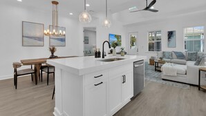 A modern kitchen with a central island, white cabinetry, and pendant lighting. - Saona Cottage - Coastal Elegance (Naples)