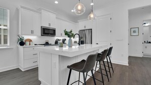 A modern kitchen with white cabinetry, a central island with bar stools, a microwave, and a refrigerator. - Saona Cottage - Coastal Elegance (Naples)