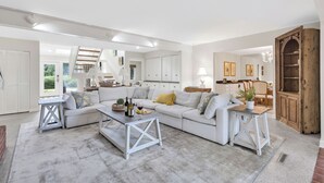 A spacious living room with a white sofa, a coffee table, and a dining area with wooden furniture.