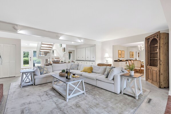 A spacious living room with a white sofa, a coffee table, and a dining area with wooden furniture.