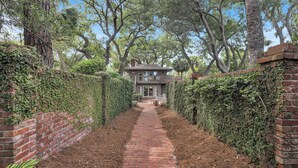 A brick pathway leading to a house surrounded by lush greenery and trees.