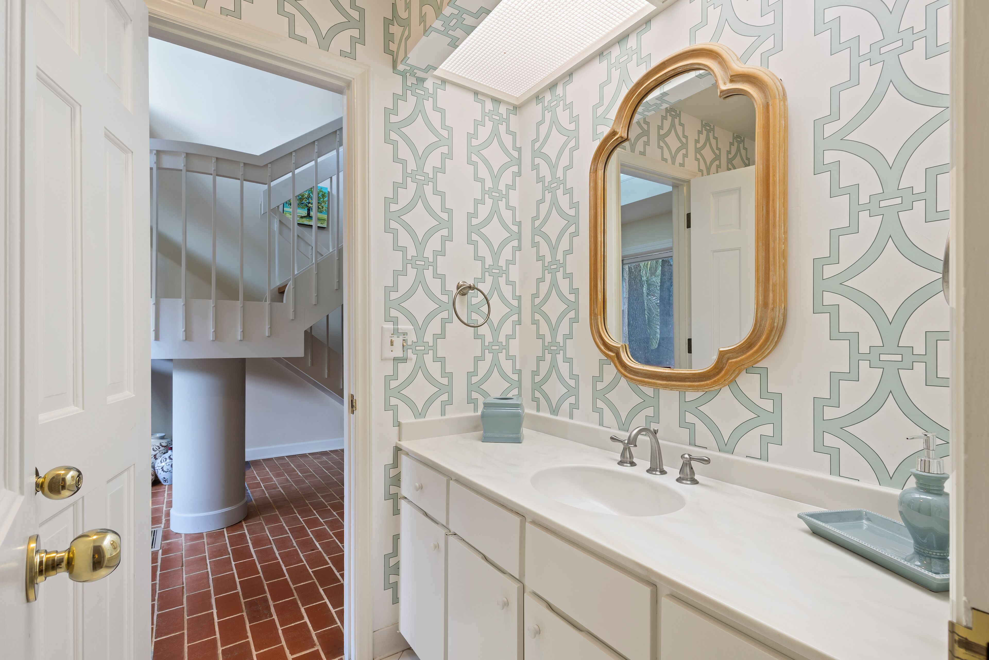 A bathroom with a white vanity, a large mirror, and patterned wallpaper.