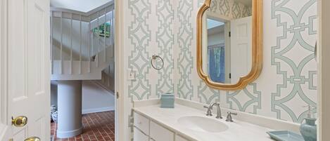 A bathroom with a white vanity, a large mirror, and patterned wallpaper.