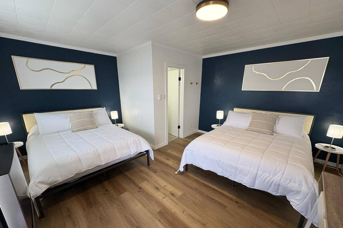 A hotel room with two beds, wooden flooring, and artwork on the walls.