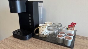 A coffee maker with a drip tray, a mug, a glass container, and a coffee pod holder.