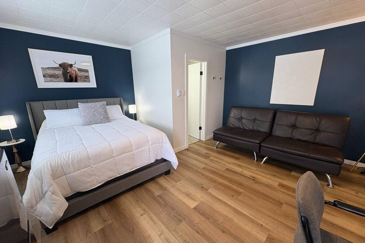 A bedroom with a bed, a sofa, a chair, and a picture on the wall.