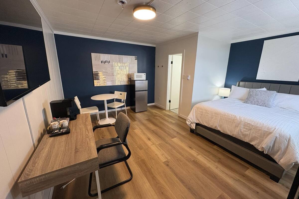 A hotel room with a bed, a desk with chairs, a microwave, and a refrigerator.