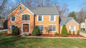 A two-story brick house with a front porch, multiple windows, and a well-maintained lawn. - Luxurious Dream Home For 10! (Loveland)