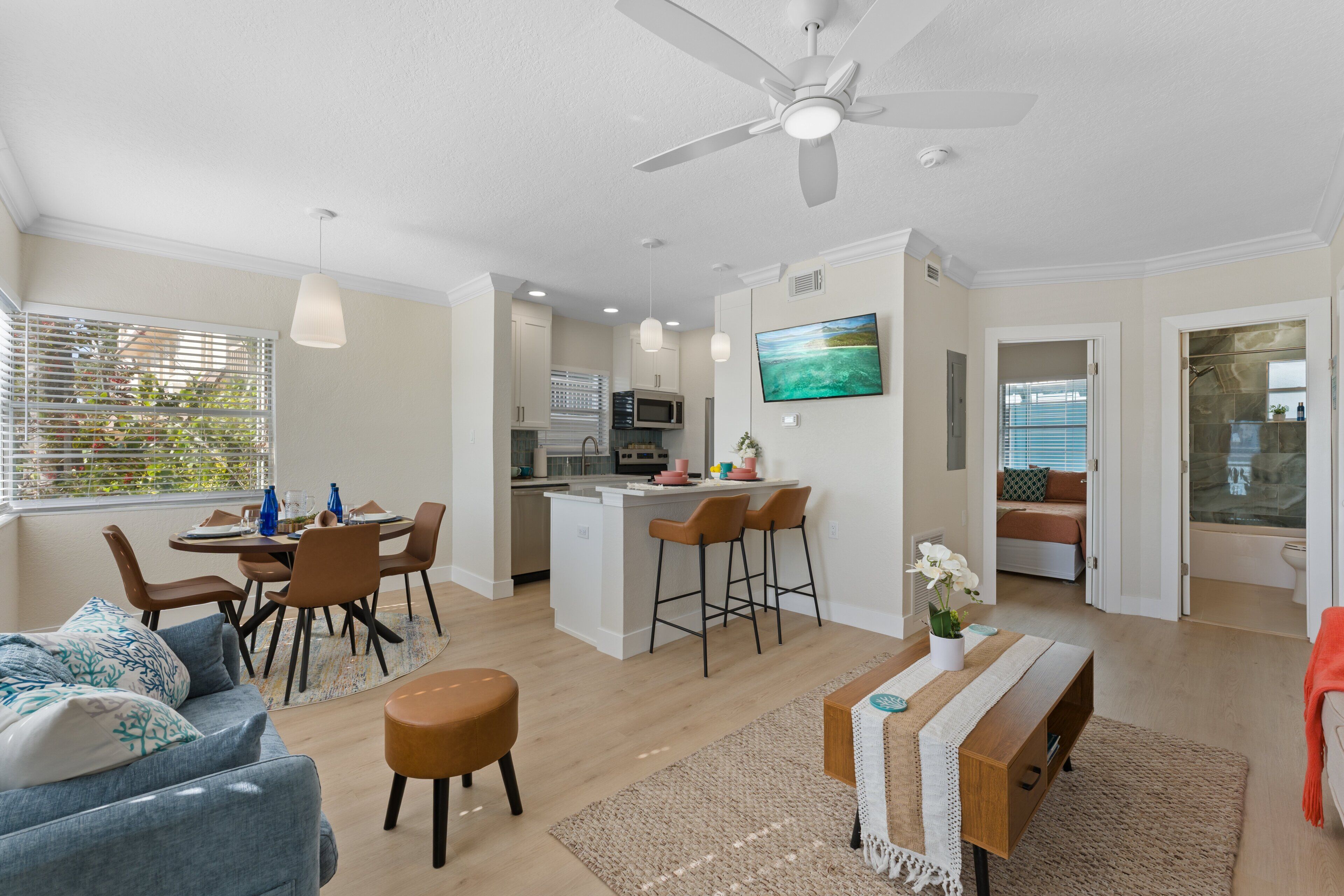 A modern living room with a dining area, kitchen, and a bedroom with a shower.