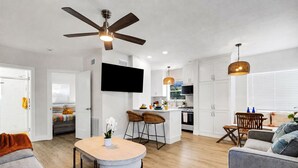 A modern living room with a dining area, kitchen, and a TV mounted on the wall.