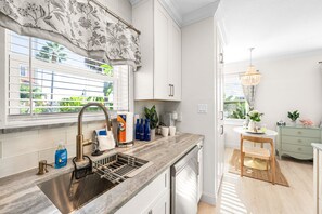 Eine moderne Küche mit einer Edelstahl-Spüle, einem Fenster mit Blumenmuster und Blick auf Grünfläche.