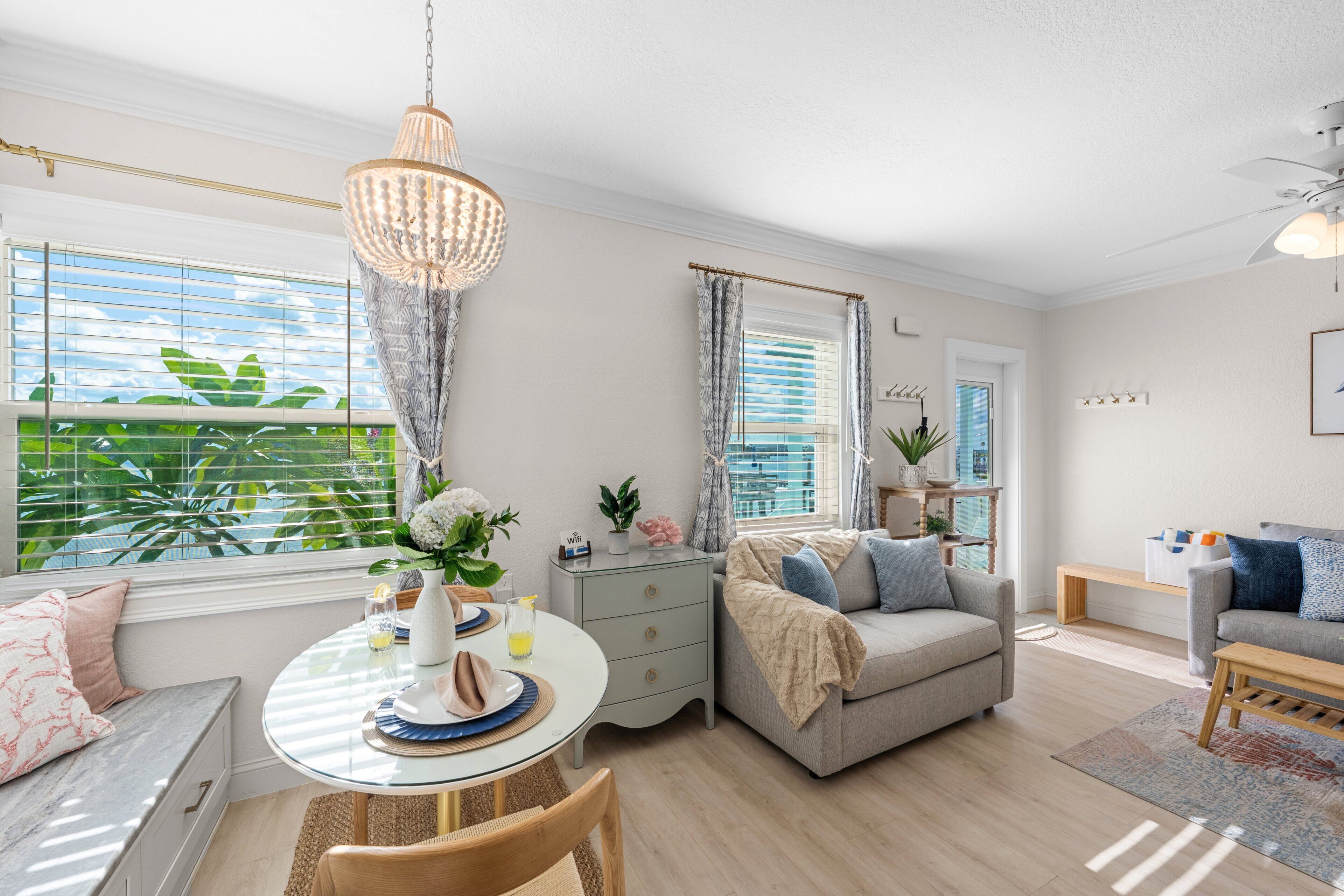 A modern living room with a dining area, a grey sofa, a round table with a glass top, and a chandelier.