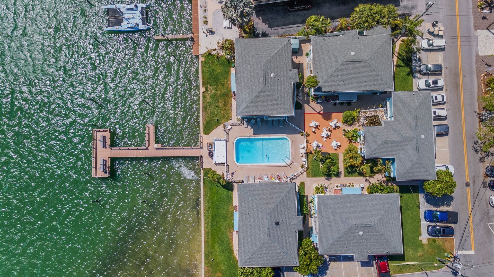 An aerial view of a coastal property with a swimming pool, multiple houses, and a dock with boats.
