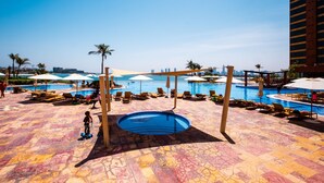 A pool area with lounge chairs and umbrellas, a small pool, and a view of the city skyline. - 2BR at the Palm | Balcony, Pool, Gym & Beach (Dubai)
