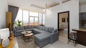 A modern living room with a sectional sofa, a round coffee table, and a dining area with stools. - 2BR at the Palm | Balcony, Pool, Gym & Beach (Dubai)