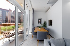 A modern living room with a wooden dining table, grey sofas, and a balcony with wicker chairs.
