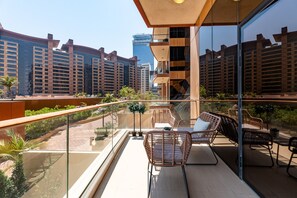 A modern balcony with wicker furniture, glass railings, and a view of surrounding high-rise buildings. - 2BR at the Palm | Balcony, Pool, Gym & Beach (Dubai)