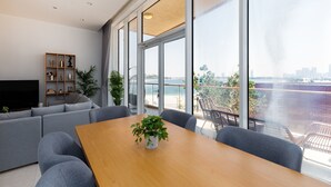 A modern living room with a large wooden table, grey sofas, and a television. - 2BR at the Palm | Balcony, Pool, Gym & Beach (Dubai)