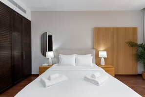A hotel room with a large bed, two bedside tables with lamps, a wooden headboard, a large mirror, and a potted plant. - 2BR at the Palm | Balcony, Pool, Gym & Beach (Dubai)