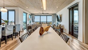 Een moderne eetruimte met een lange tafel, stoelen en een uniek houten sculptuur als middelpunt.
