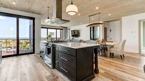 Een moderne keuken met een groot eiland, houten vloeren en grote ramen met uitzicht op de omgeving.