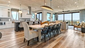 Een moderne keuken met witte kasten, een eethoek met een witte tafel en stoelen, en een groot raam met uitzicht op de oceaan.