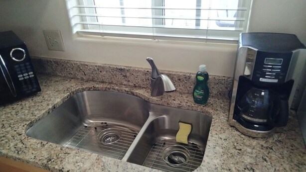 A kitchen with a double sink, a coffee maker, and a bottle of dish soap.