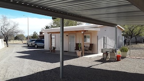 A small, single-story building with a covered patio area. There are two cars parked in the driveway, and a person is visible in the background.
