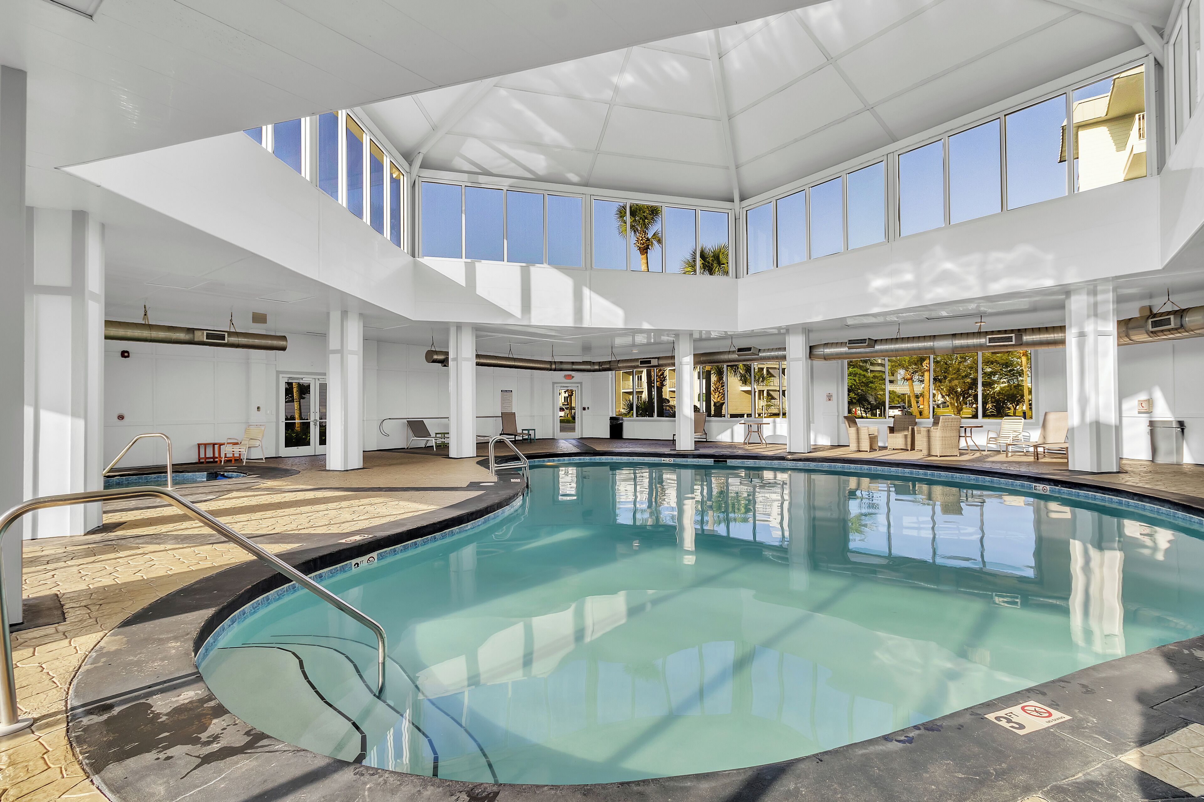 An indoor swimming pool with clear blue water, surrounded by white pillars and a high ceiling with skylights.