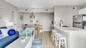 A modern kitchen with white cabinetry, a stainless steel refrigerator, and a bar area with white stools. - Flash Sale 2BR/2BA Gulf View | Sleeps 8 (Gulf Shores)