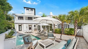Una casa de dos pisos con piscina, mobiliario exterior y una cerca blanca.