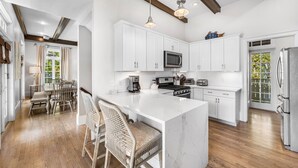 Una cocina moderna con muebles blancos, una isla central y un comedor con sillas de madera.