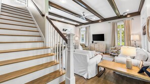 Una escalera con escalones de madera y barandillas blancas, un salón con un sofá blanco, una mesa de centro y una televisión.