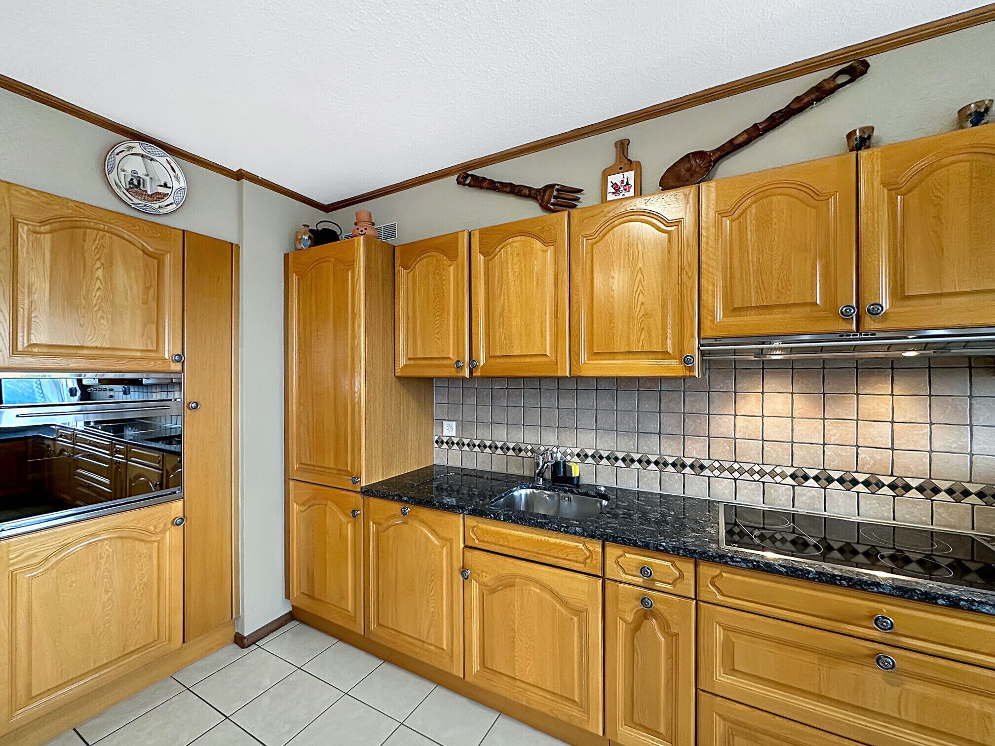 Una cocina con armarios de madera, encimera negra y salpicadero de azulejos.