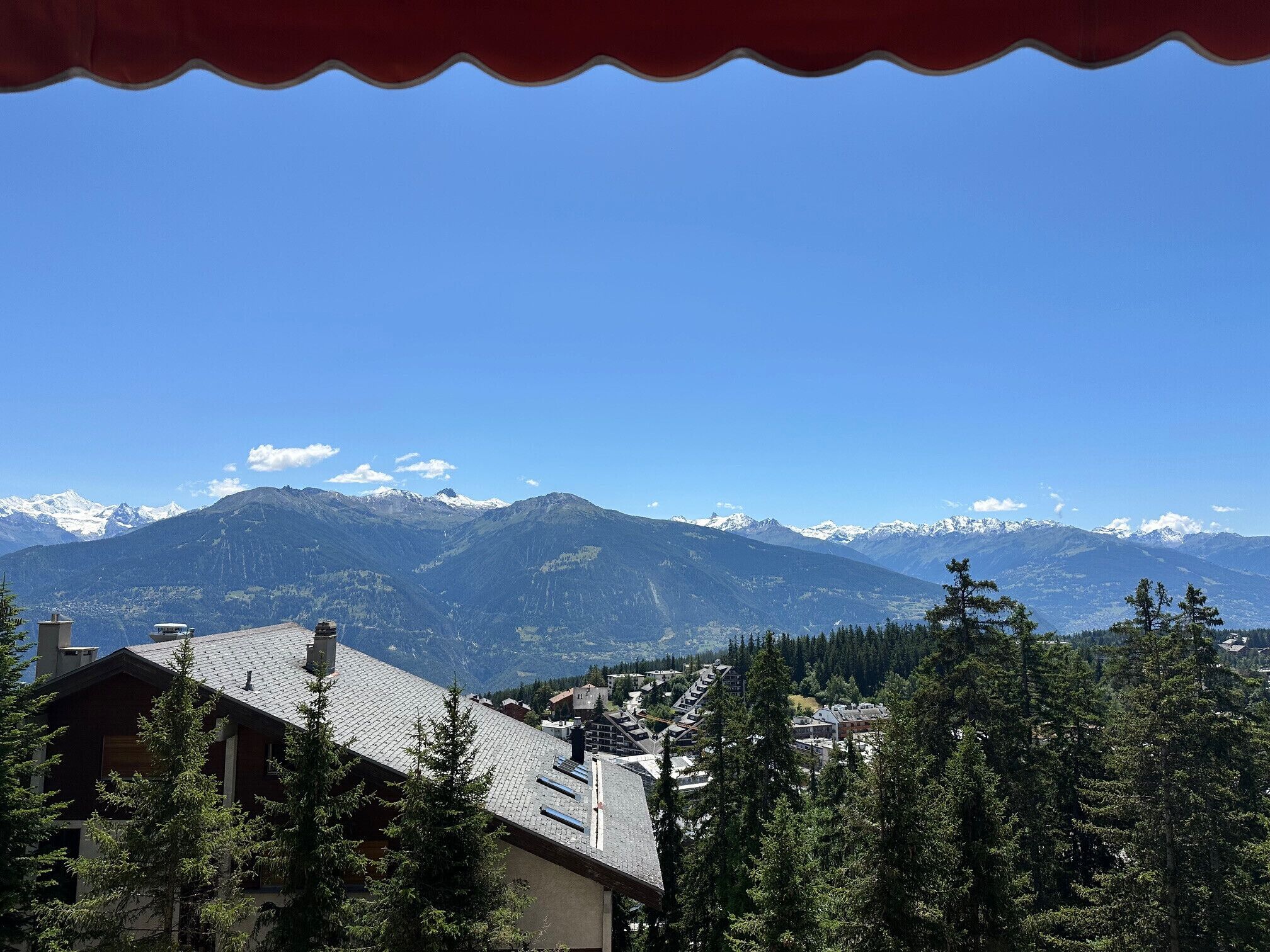 A mountain landscape with snow-capped peaks, a town with buildings, and dense forest in the foreground.