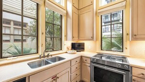 Una cocina con un lavamanos doble, estufa, horno y un televisor sobre la encimera.