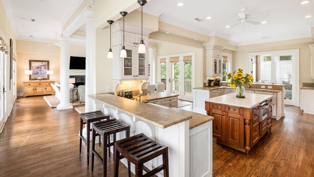 A spacious kitchen with a large island, wooden bar stools, pendant lighting, and a view of the outdoors.