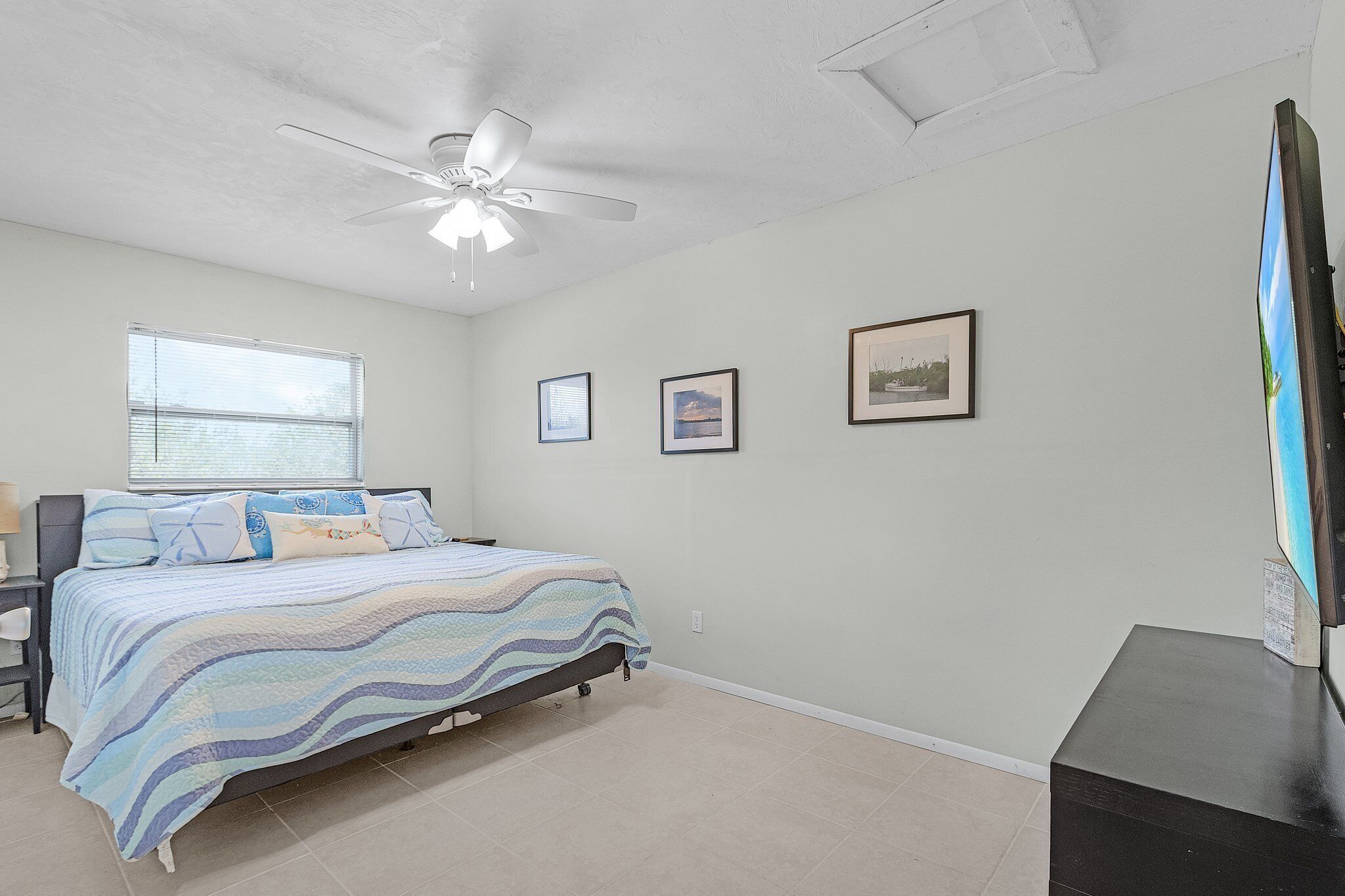A bedroom with a bed, ceiling fan, framed pictures, and a TV.